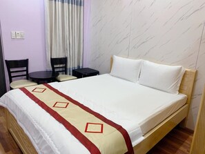 Une chambre d’hôtel avec un lit, une petite table, deux chaises et une fenêtre avec des rideaux.