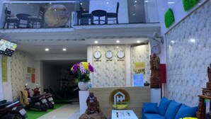 A spacious, modern interior with a two-level layout, featuring a balcony with seating, a reception area with a sofa and decorative items, and a clear view of the sky through a large window. - Hung Phat Hotel (Ho Chi Minh City)