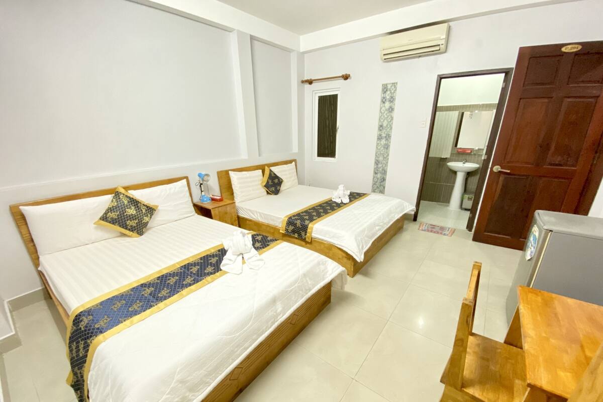 A hotel room with two beds, a wooden chair, a desk, a sink, and an air conditioning unit.