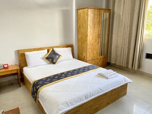 Ein ordentlich bezogenes Bett mit blauer und goldener Bettdecke, ein Holfschrank und ein Nachttisch mit Telefon.