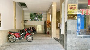 A hallway with a row of motorcycles parked on the left, a large poster on the wall, and a clock on the right. - Thien Son Hotel (Ho Chi Minh City)