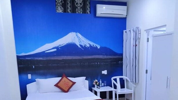 A bedroom with a bed, a nightstand, a chair, and a wall mural of a mountain. - An Binh Hotel (Ho Chi Minh City)