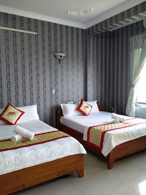 A hotel room with two wooden beds, striped wallpaper, and a window with curtains.