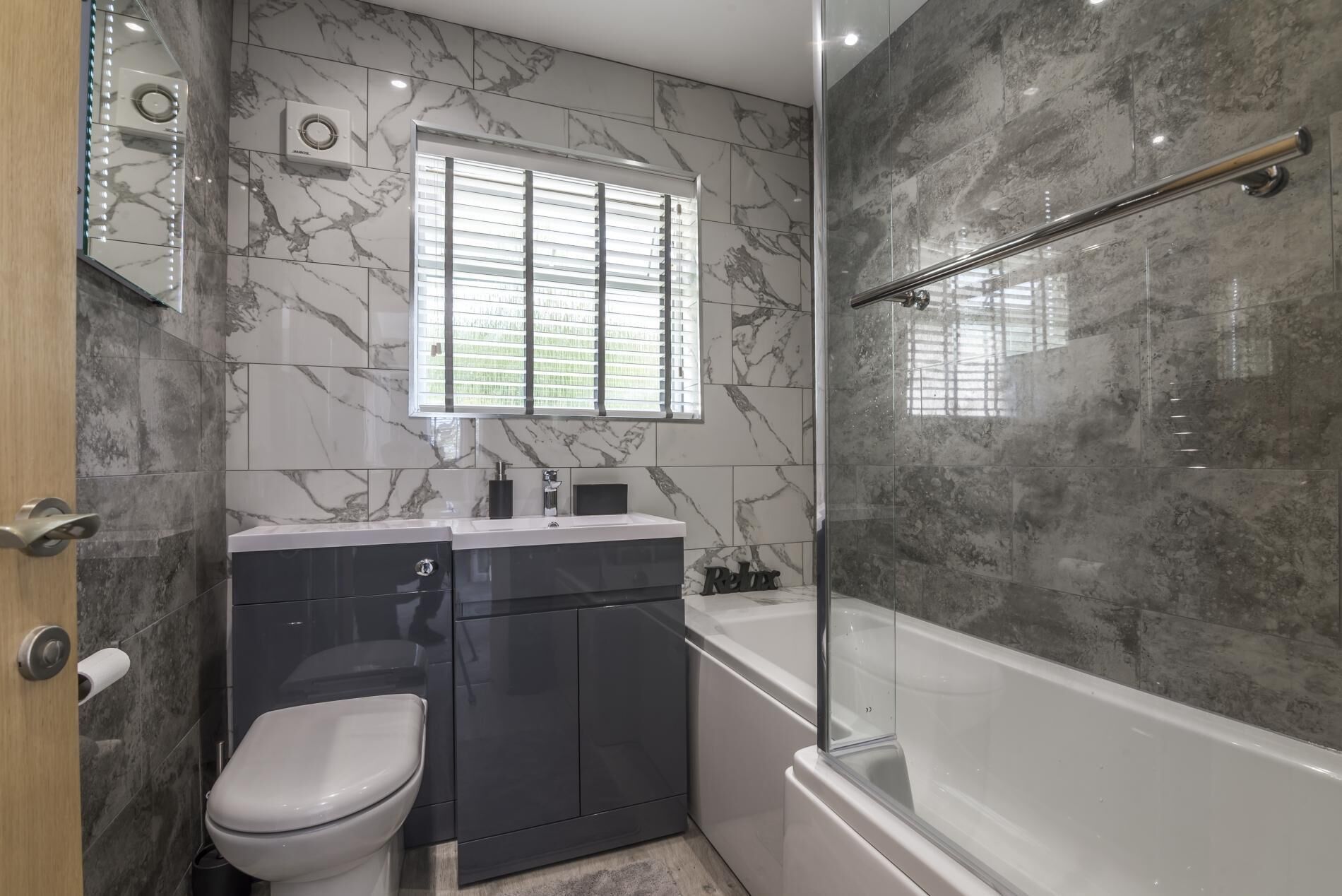 A modern bathroom with a marble backsplash, a toilet, a vanity with a mirror, and a walk-in shower.
