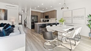 Una cocina moderna con una isla central, electrodomésticos de acero inoxidable y un comedor con una mesa y sillas blancas.