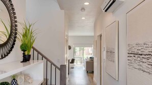 Un couloir moderne avec un escalier, une plante en pot et des œuvres d’art accrochées aux murs.
