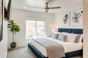 A bedroom with a bed, a ceiling fan, a window, and a potted plant.