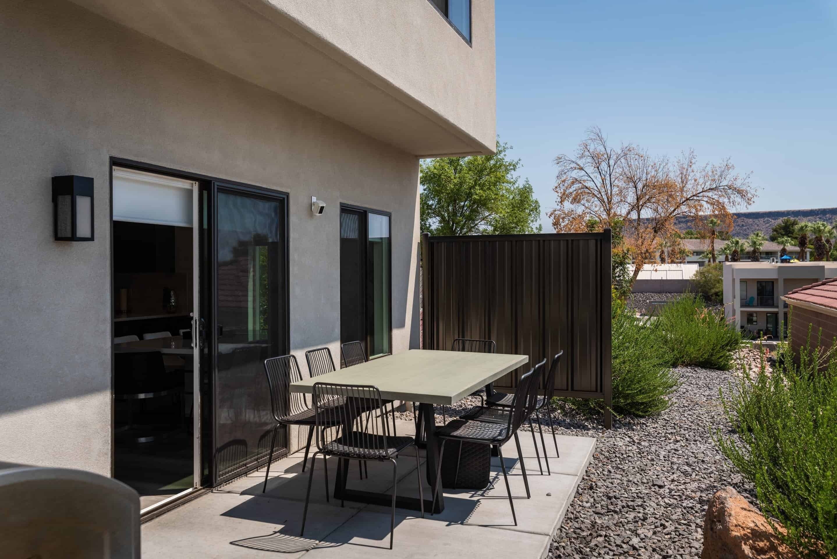 A patio with a table and chairs, a sliding glass door, and a view of a building and trees in the background.
