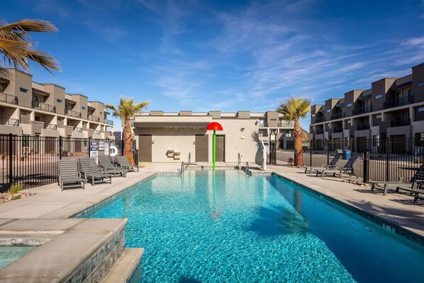 Relax by the pool surrounded by comfortable lounge chairs and two-story buildings with balconies.