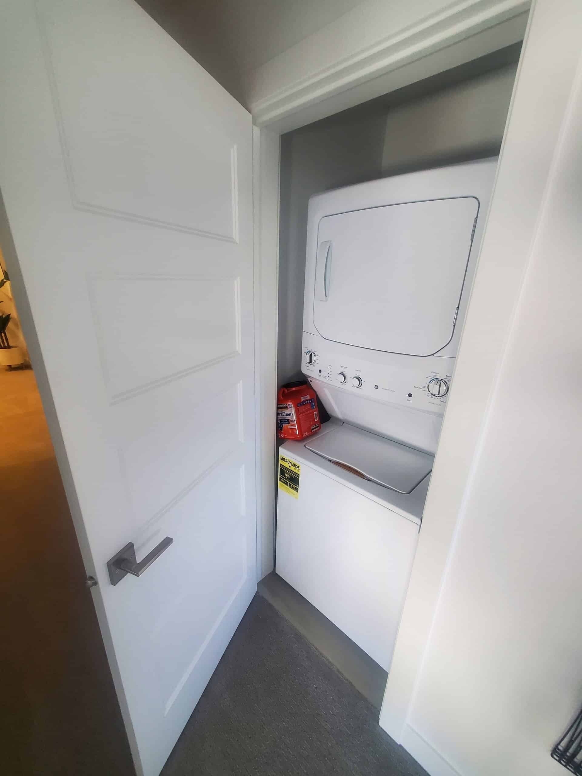 A laundry room with a white washing machine, a dryer, and a red cleaning product bag.