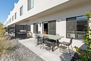 A modern outdoor patio with a dining table and chairs, a grill, and a covered seating area.