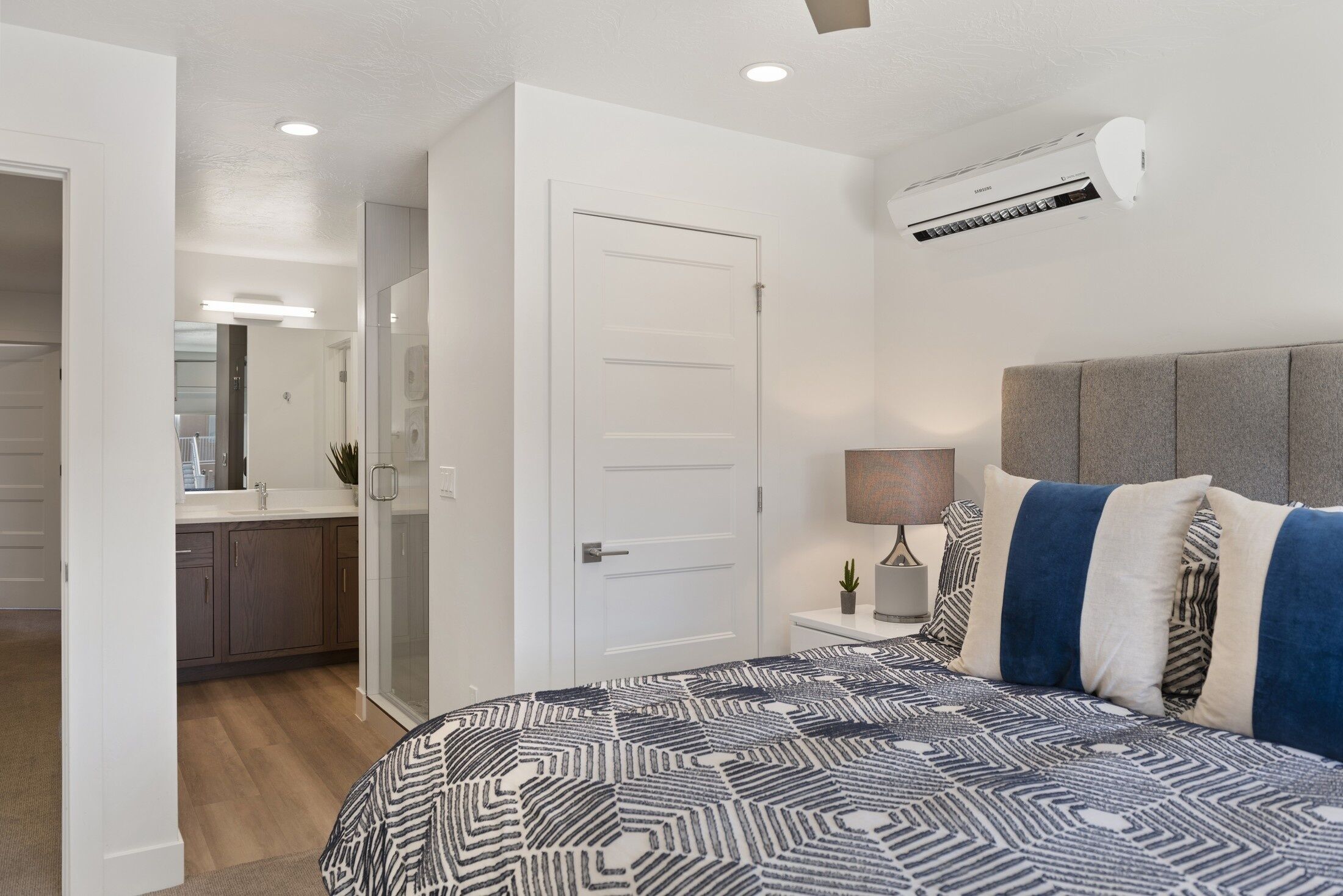 A bedroom with a patterned bedspread, a bedside lamp, and a wall-mounted air conditioner.