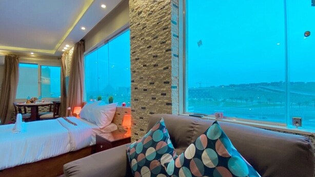 A hotel room with a large bed, a sofa with patterned cushions, a dining table, and a view of the cityscape. - Deluxe Studio with amazing Pyramids view (Giza)