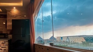 A modern kitchen with a large window, a stone wall, and a black refrigerator. - Deluxe Studio with amazing Pyramids view (Giza)