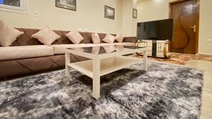 A living room with a sofa, a coffee table, a flat-screen TV, and a patterned rug. - Deluxe Studio with amazing Pyramids view (Giza)