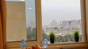 A dining table with various dishes and a view of pyramids through a window. - Deluxe Studio with amazing Pyramids view (Giza)
