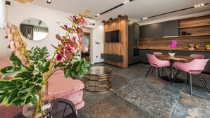 A modern living room with a pink sofa, a round glass coffee table, and a dining area with pink chairs and a wooden table. - Villa Laverna (Novalja)