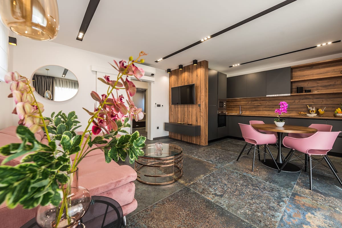 Una sala moderna con un sofá rosa, una mesa de centro redonda de vidrio y una zona de comedor con sillas rosas y una mesa de madera.