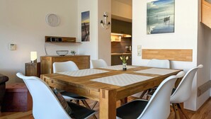A dining area with a wooden table, white chairs, a clock, and a painting on the wall. - Papillon Wohnung 08-7 (Ostseebad Boltenhagen)