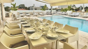 Un área de comedor al aire libre con vista a la piscina, mobiliario blanco y una sección cubierta.