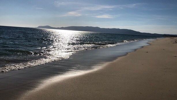 Una playa con cielo despejado y luz del sol reflejada en el agua.
