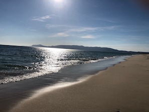 Una platja amb cel blau i reflexos de sol a l'aigua.