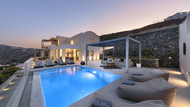 Una villa moderna con piscina, mobiliario de exterior y un muro de piedra.