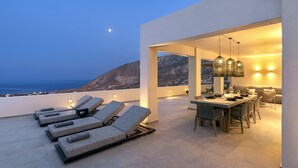Una terraza en la azotea con sillones de descanso, un comedor con mesa y sillas, y vistas al mar y a las montañas.