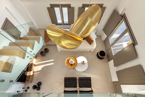 A modern interior with a glass staircase, a hanging gold-colored light fixture, and a seating area with black and white cushions. - Eolia Gold Villa with Private Heated Pool (THIRA, SANTORINI)