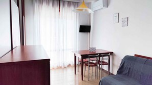 Una camera d'albergo con una scrivania in legno, un divano grigio e un tavolo da pranzo con sedie.