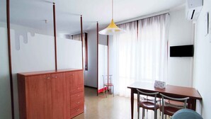Una camera d'albergo moderna con un'armadio in legno, un tavolo da pranzo con sedie, un divano e un'ampia finestra con tende.