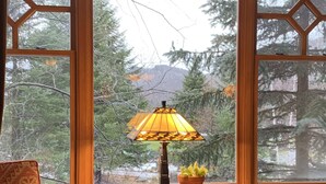 A cozy room with a large window, a table with a lamp, and a chair.