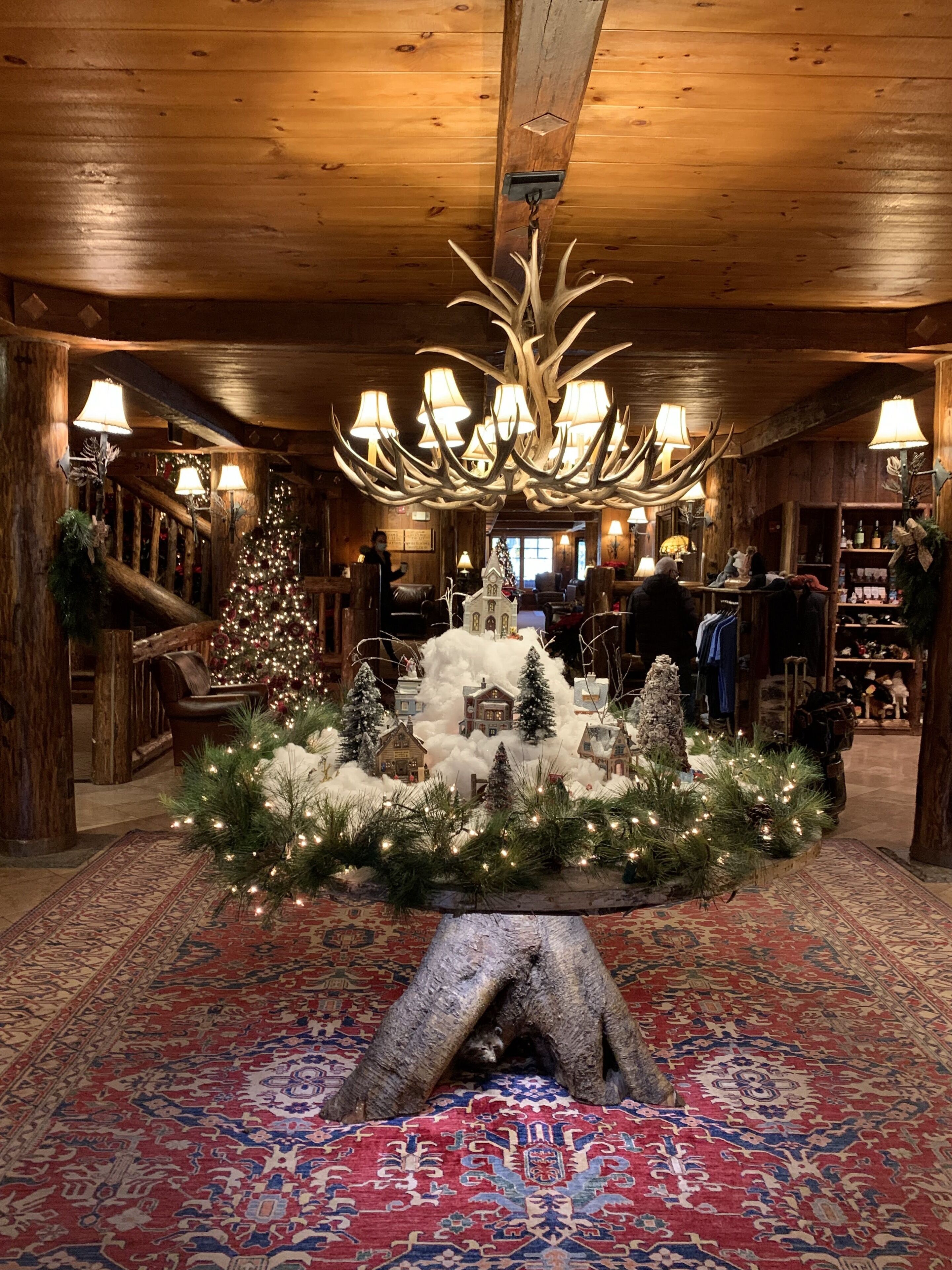 A warmly lit lobby with a large antler chandelier, a Christmas tree, and a rustic fireplace.