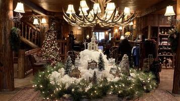A warmly lit lobby with a large antler chandelier, a Christmas tree, and a rustic fireplace.