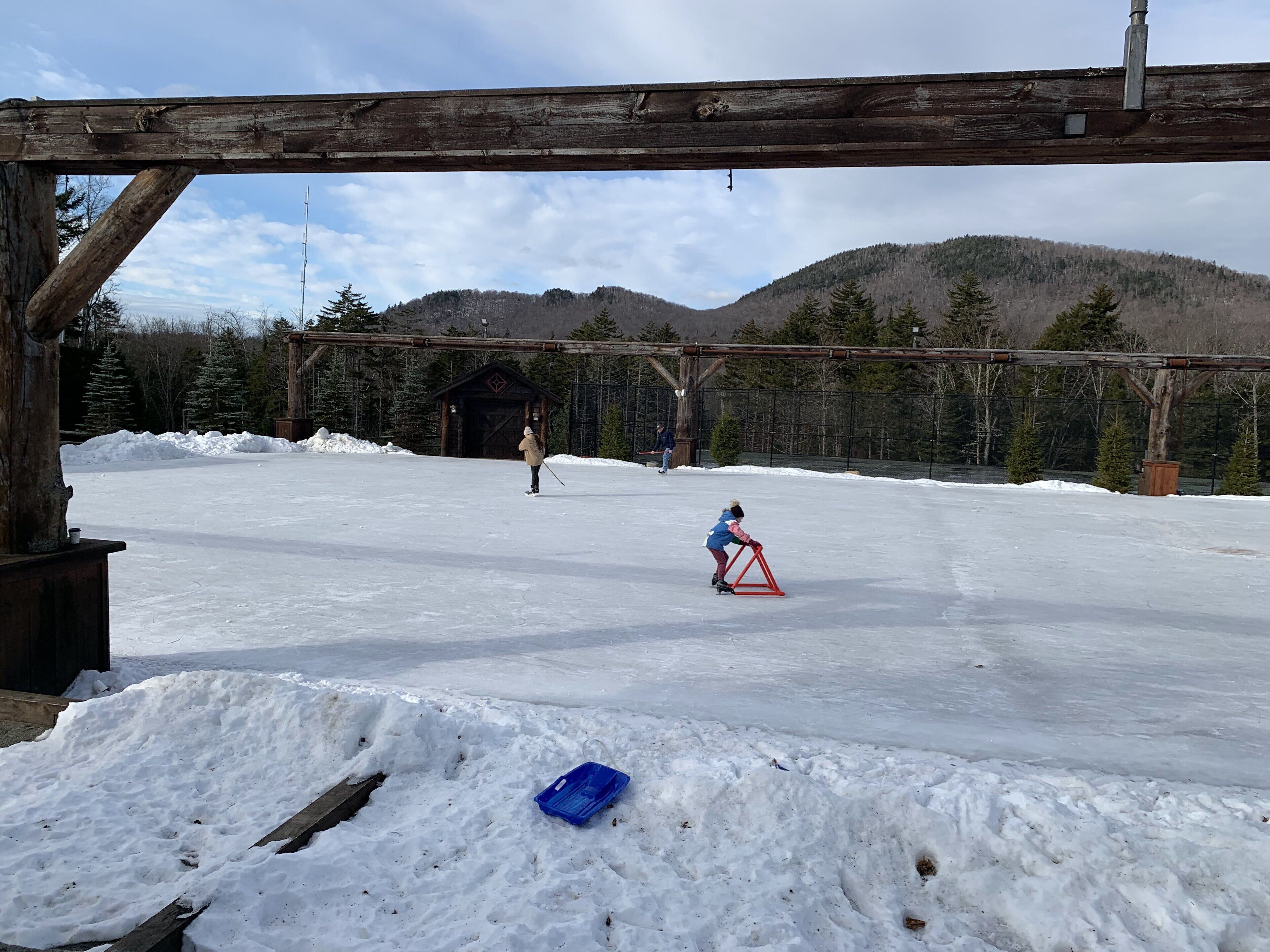 A snowy outdoor area with a wooden structure, a small building, and a person on skis.