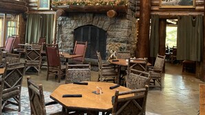 A rustic lodge interior with a stone fireplace, wooden furniture, and a deer head mounted on the wall.