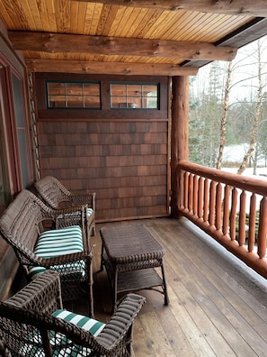Une terrasse en bois, meublée de meubles en osier, notamment des chaises et une table, et offrant une vue sur un paysage enneigé.
