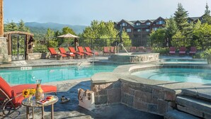 A pool area with lounge chairs, a hot tub, and a view of mountains.