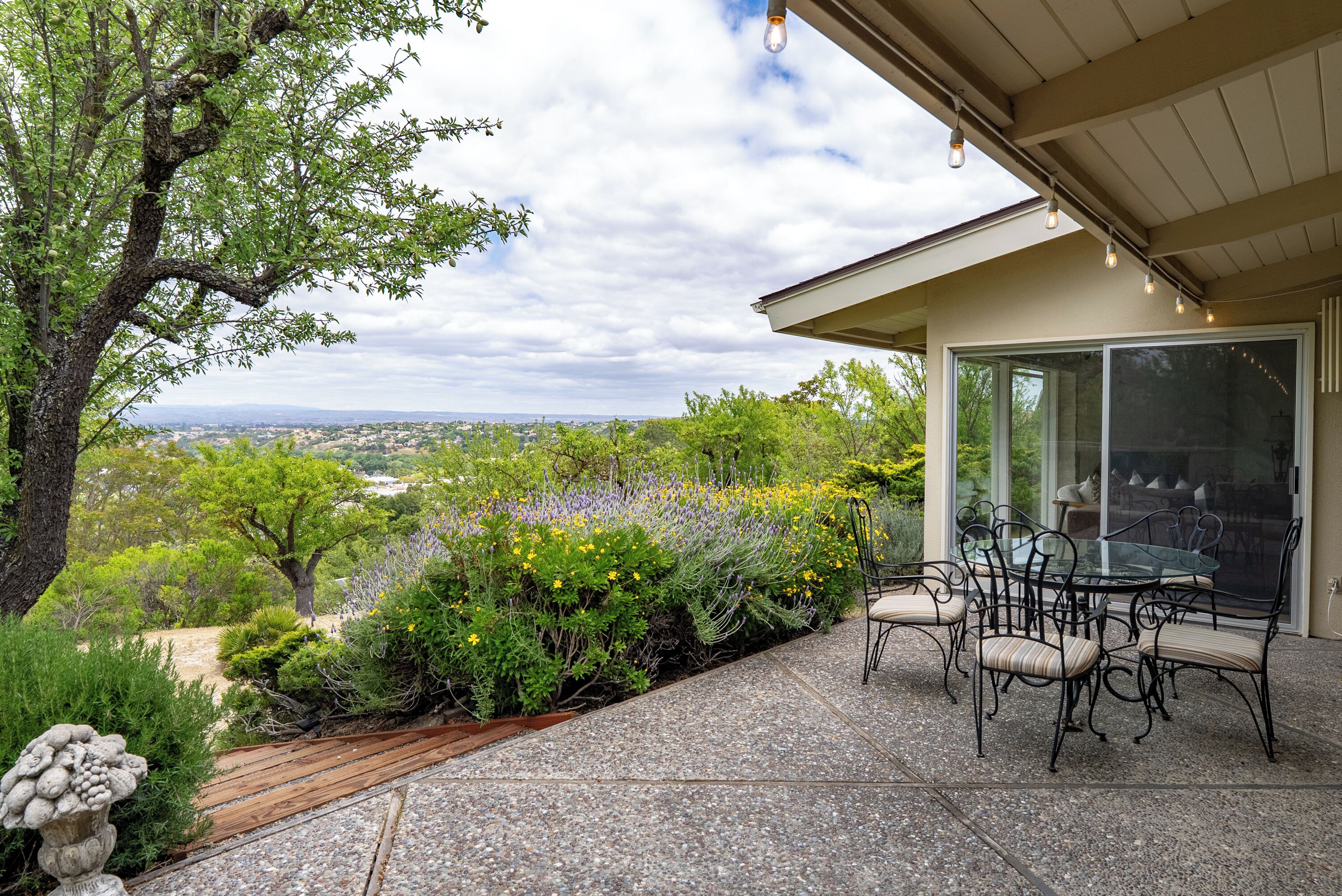 A patio with a table and chairs, surrounded by greenery and a view of the landscape.