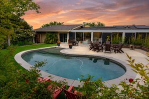 Piscina residencial de diseño curvo, rodeada por un patio con mobiliario exterior.
