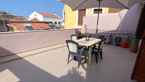 An outdoor patio with a table and chairs, a large umbrella, and potted plants. - Casa Dasyra (Chania)