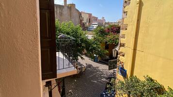 Un callejón estrecho con un edificio amarillo a la derecha, una puerta a la izquierda y una pequeña mesa con sillas en el centro.