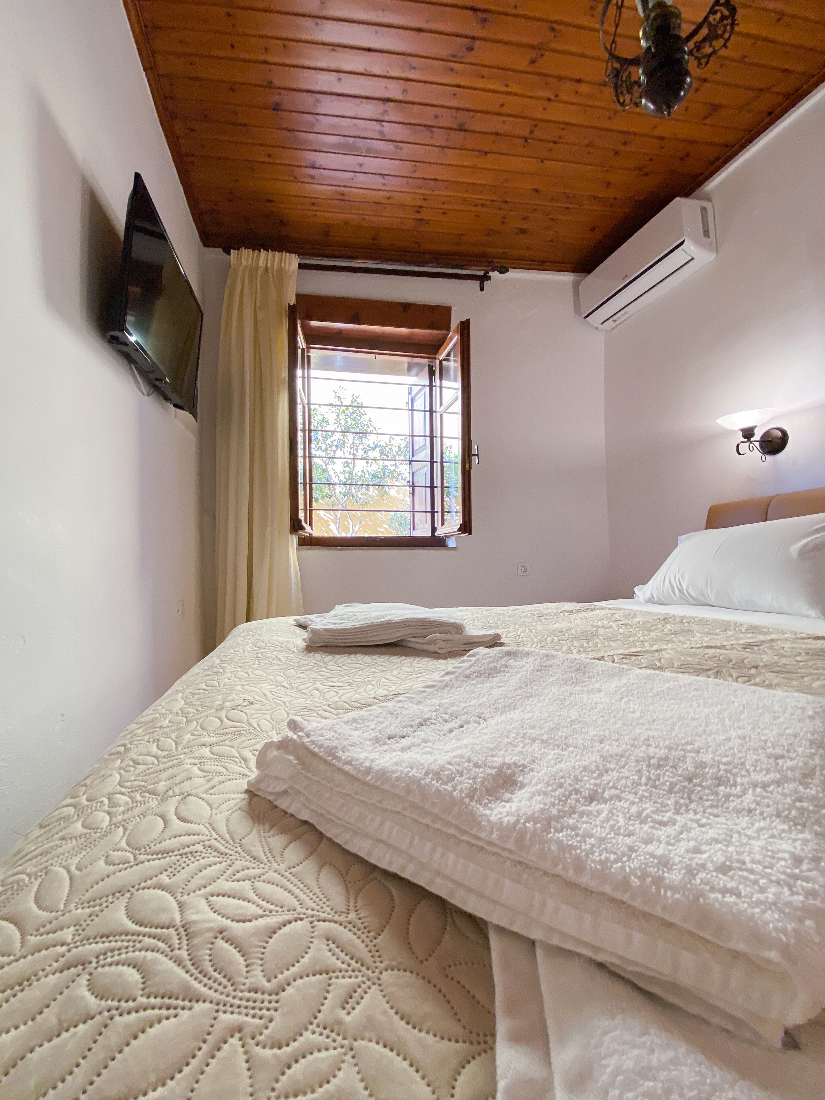 Un dormitorio con cama, ventana con cortinas, aire acondicionado y televisor montado en la pared.