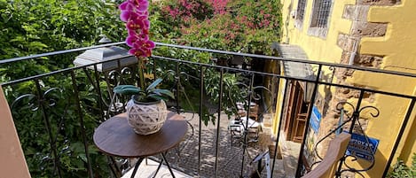 A balcony with a wooden chair and a small round table, surrounded by a metal railing.