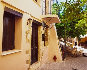 A narrow street with a building featuring a black door, a fire hydrant, and outdoor seating. - Casa Dasyra (Chania)