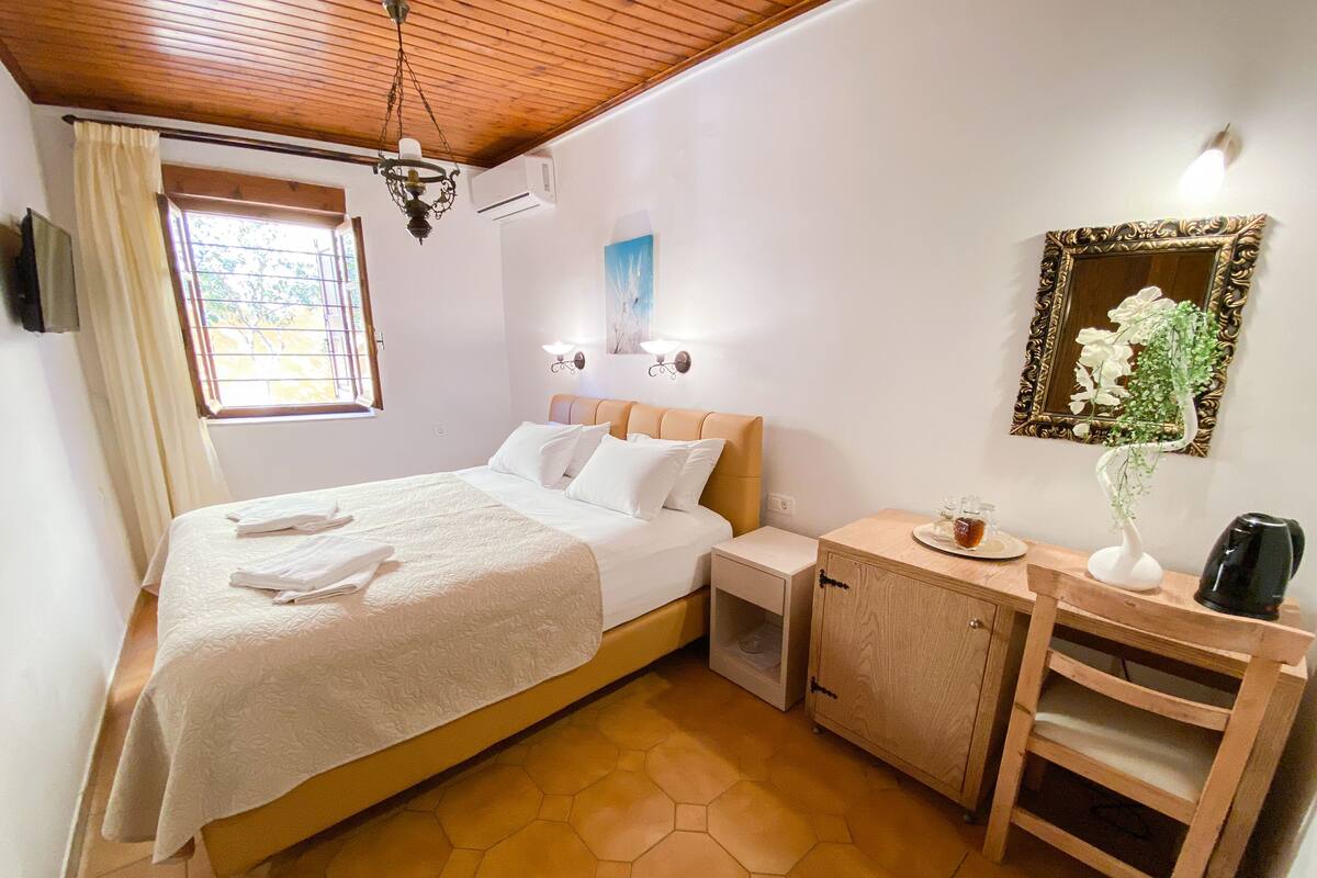 A hotel room with a bed, a wooden nightstand, a cabinet, a mirror, and a window with curtains.