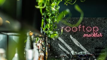 A bar area with a coffee machine, bottles, and a neon sign reading 'rooftop snackbar'.