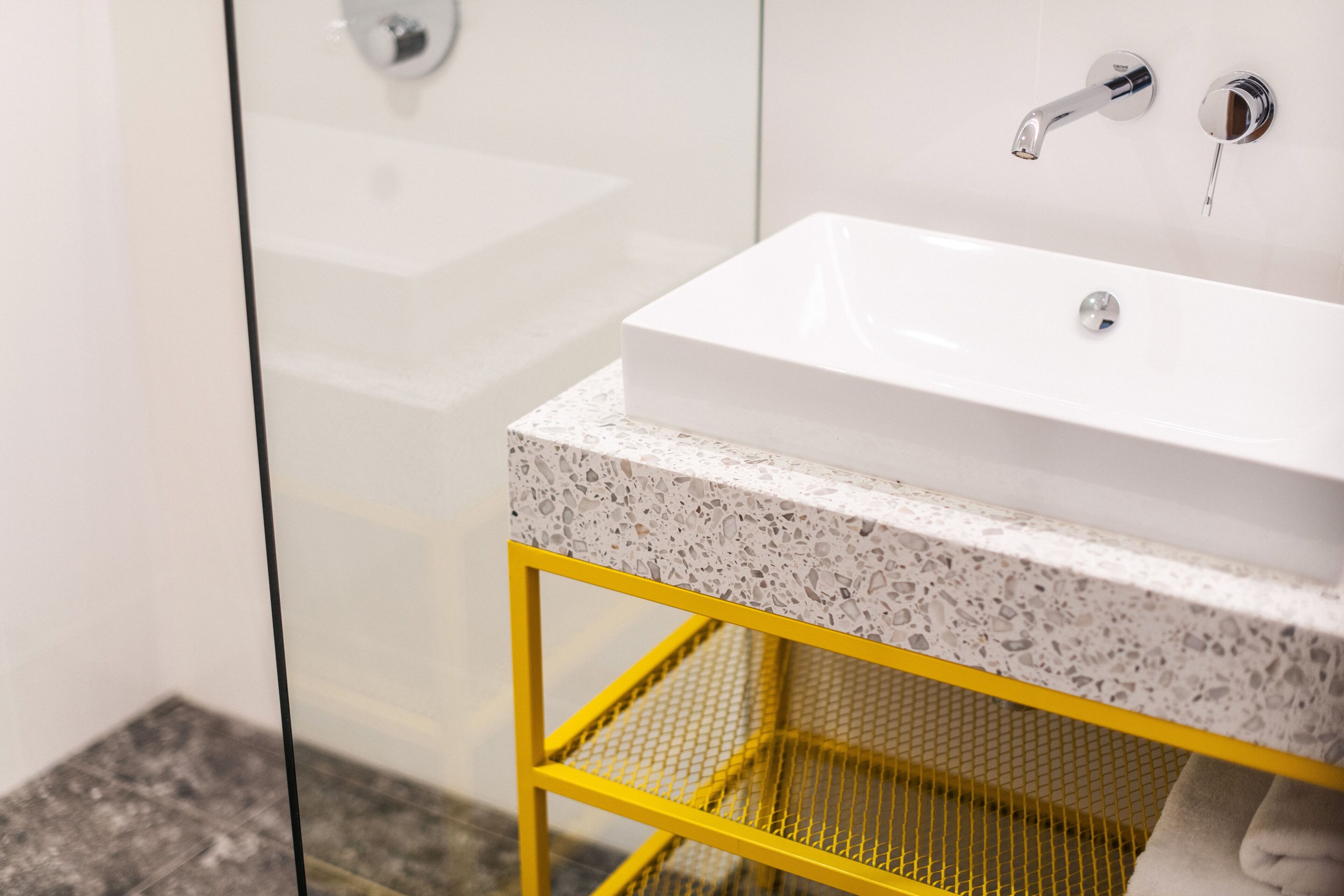 A bathroom with a white sink, a yellow metal shelf, and a glass shower enclosure.
