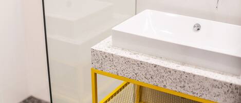 A bathroom with a white sink, a yellow metal shelf, and a glass shower enclosure.