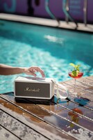 A poolside setting with a speaker and a cocktail on a wooden table.
